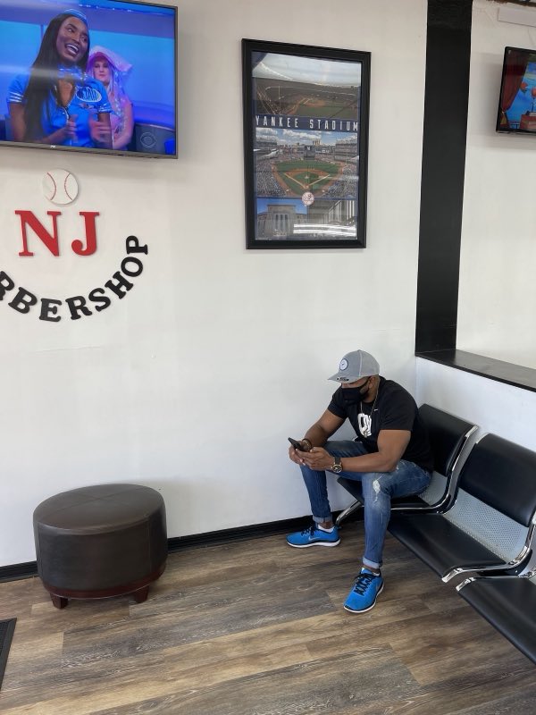Waiting area with the NJ Barbershop branded wall and TVs